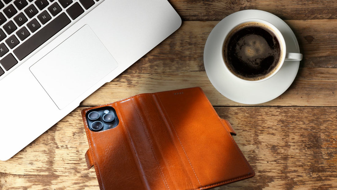 brown iPhone 16 pro max leather wallet case on top of wooden table beside a macbook and cup of coffee