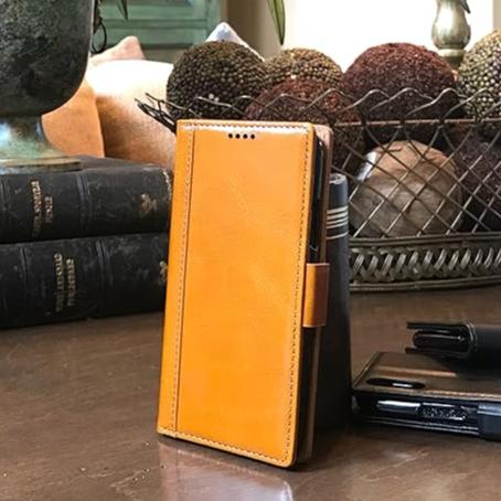 A rich cognac-colored leather wallet case with a stand for iPhone 16 pro shown on a table.