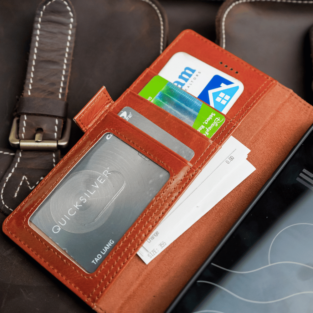 A brown leather wallet case for a Samsung Galaxy S25 ultra, standing upright on a table using its built-in kickstand. The case has multiple card slots visible.